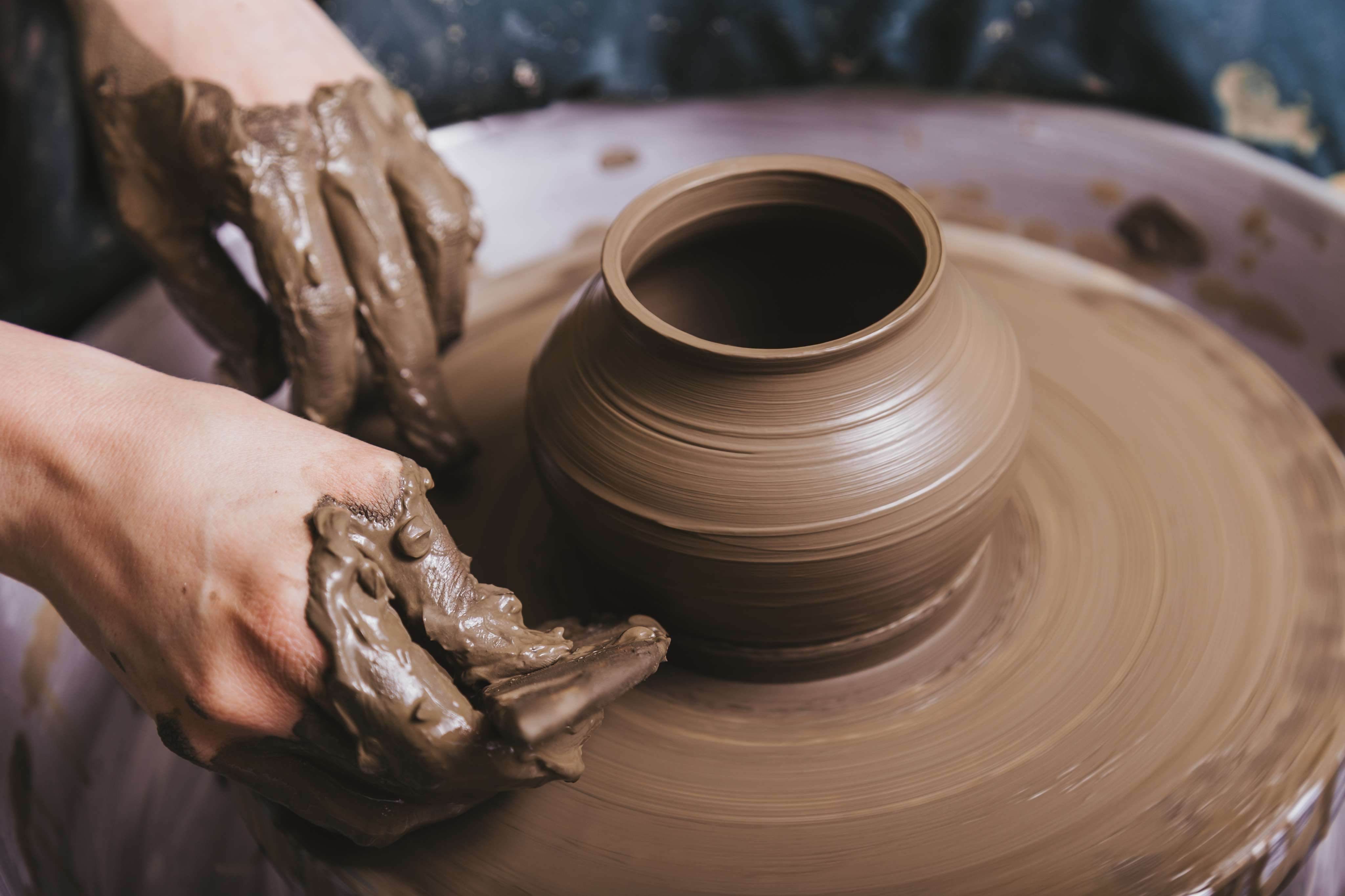 Close-up of clay-covered hands shaping a pot on a spinning pottery wheel.