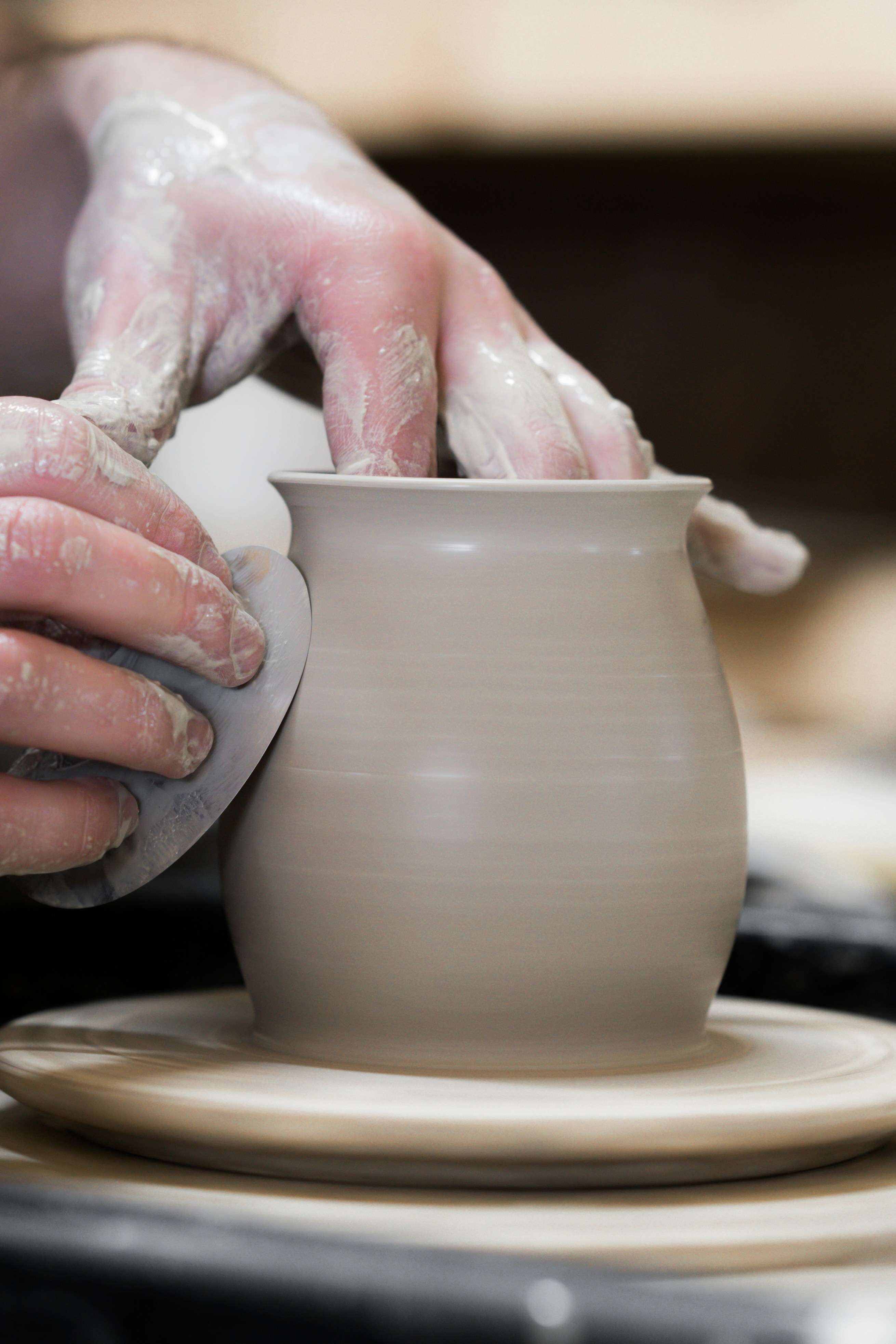 Close-up of hands smoothing the rim of a clay pot with a sponge on a pottery wheel.