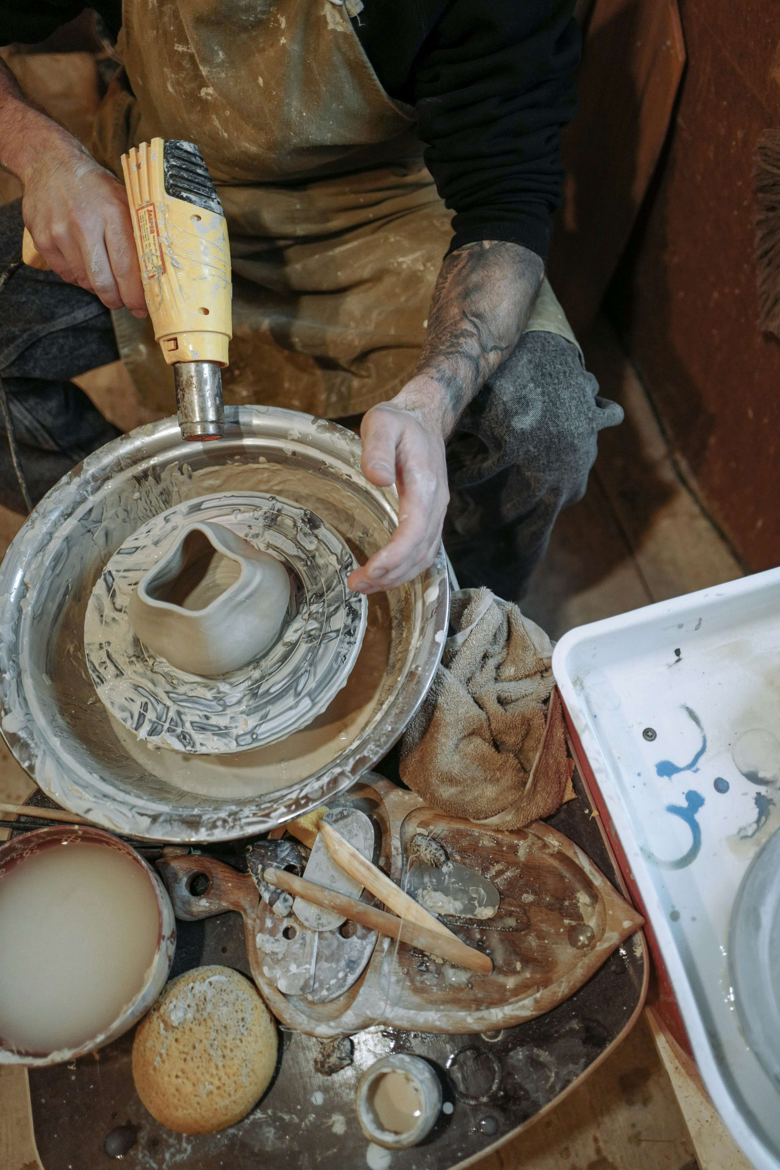 Overhead view of a tattooed potter's hands centering clay on a pottery wheel in a working studio.